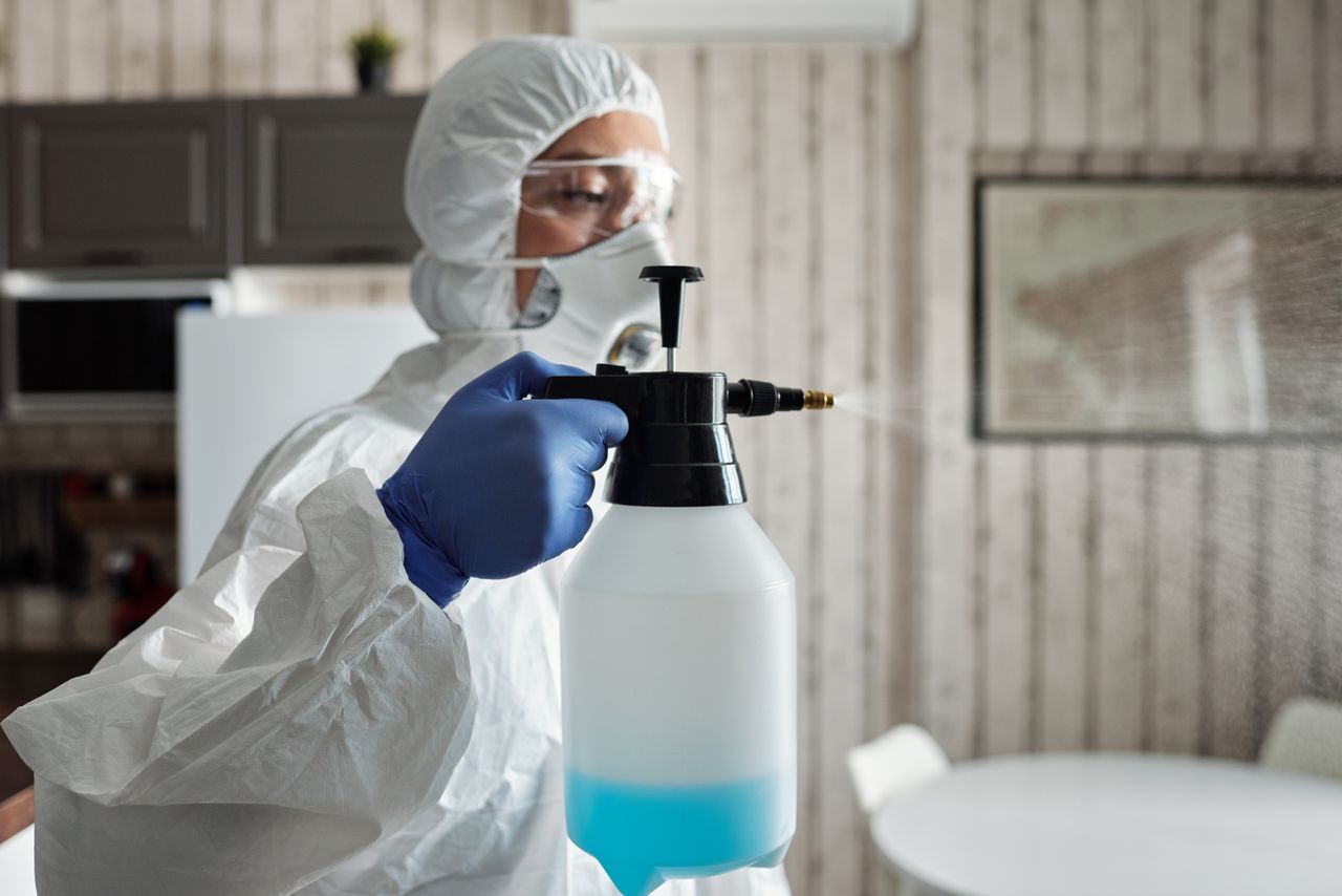 home-img Professional in full gear disinfecting indoor area using a spray bottle for COVID-19 prevention.